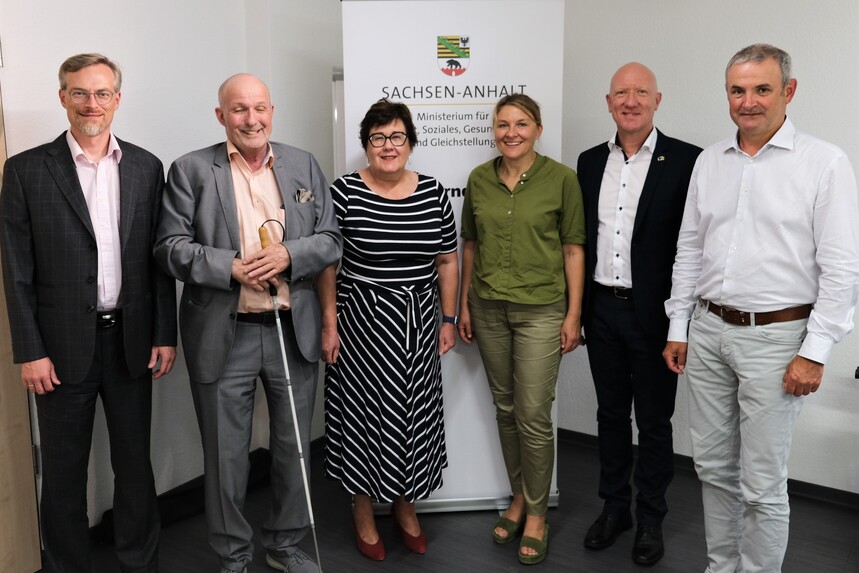 Die Behindertenbeauftragten der drei mitteldeutschen Bundesländer, stehen zusammen mit ihren Mitarbeitern und der Sozialministerin von Sachsen-Anhalt vor einem Banner. 