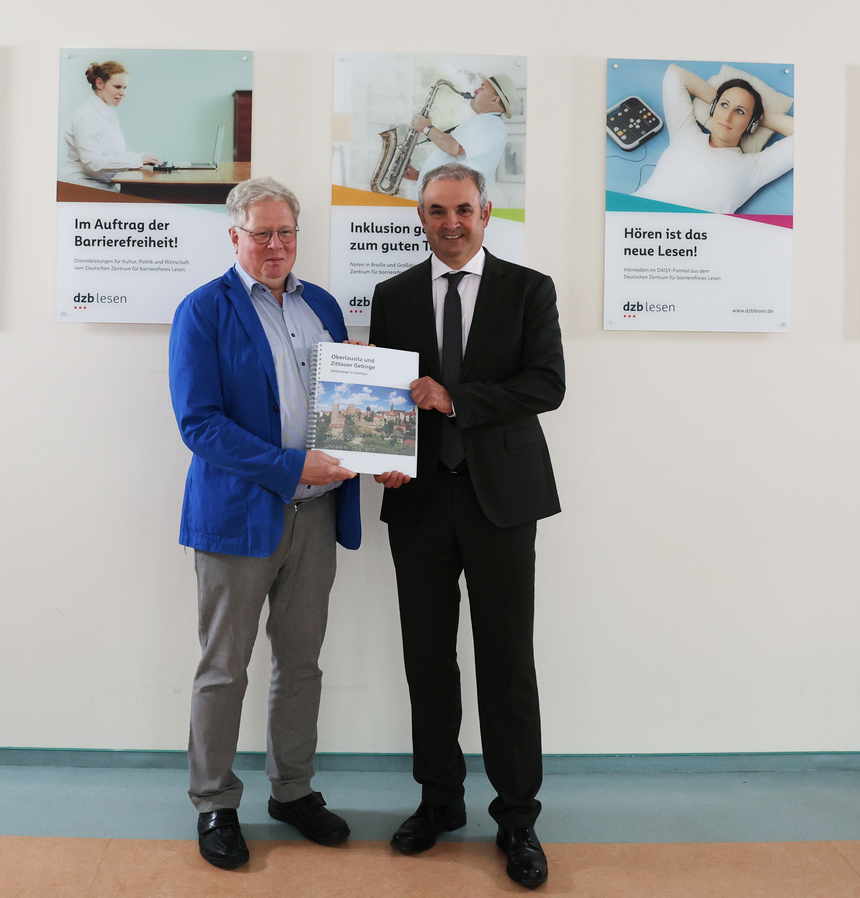 Prof. Dr. Thomas Kahlisch, Direktor des dzb lesen und der Landesbeauftragte für Inklusion der Menschen mit Behinderungen Michael Welsch stehen nebeneinander und halten gemeinsam den taktilen Tourismusführer »Oberlausitz und Zittauer Gebirge« in den Händen