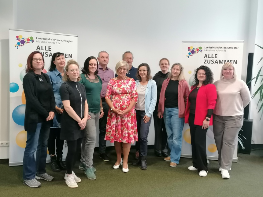 Die kommunalen Behindertenbeauftragten stehen mit dem Landesbeauftragten in einer Gruppe in einem Tagungsraum .