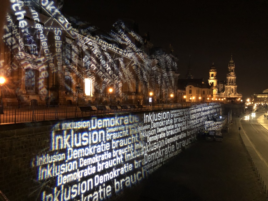 Wörter und Begriffe zur Inklusion werden durch Lichtstrahlen an die Fassade der Kunsthochschule in Dresden projiziert. 