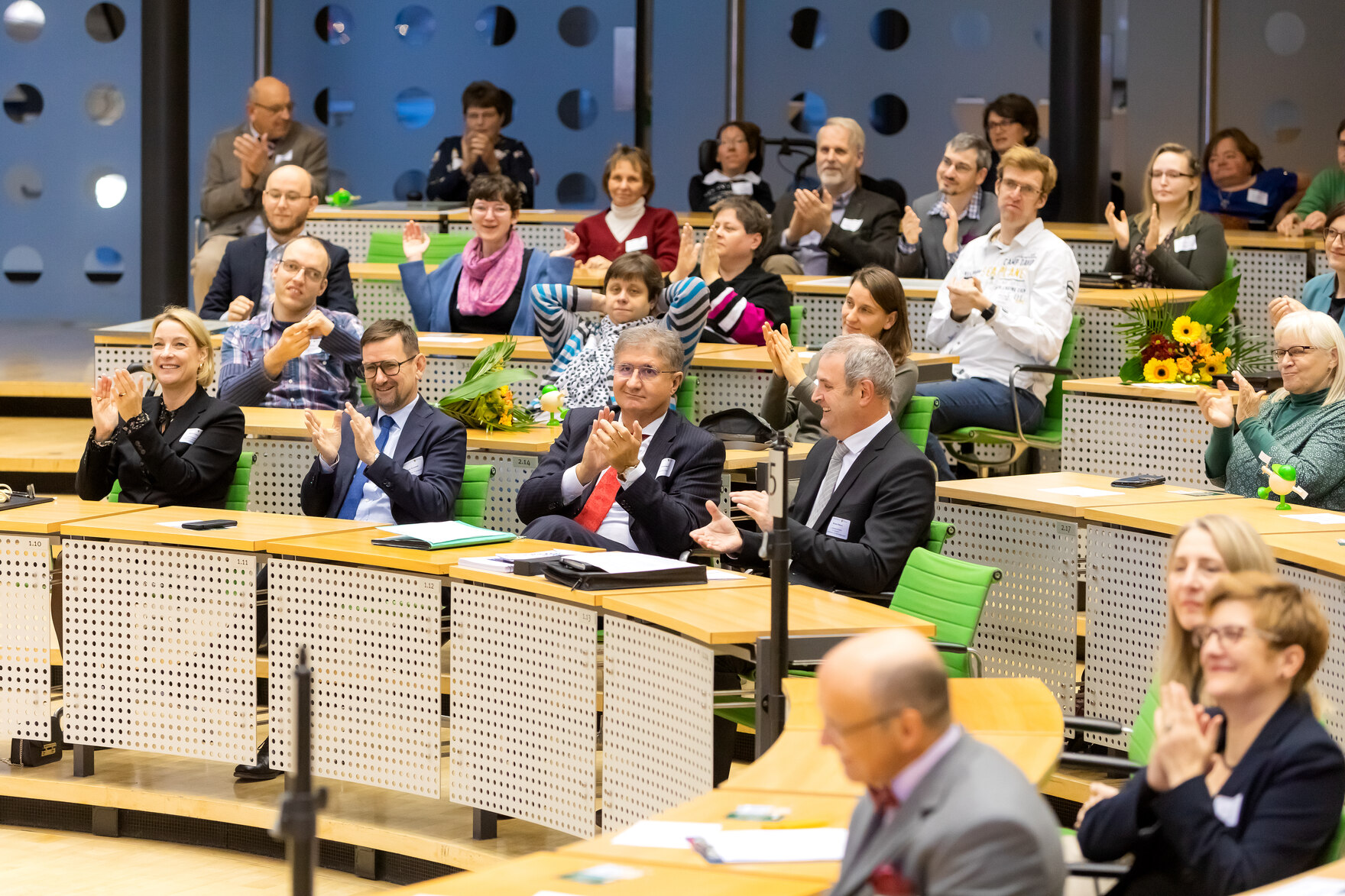 A snapshot of several participants from the prize-giving ceremony for the 5th Saxon Inclusion Award, sitting in the Chamber of the Saxon State Parliament and looking up at the executive committee.