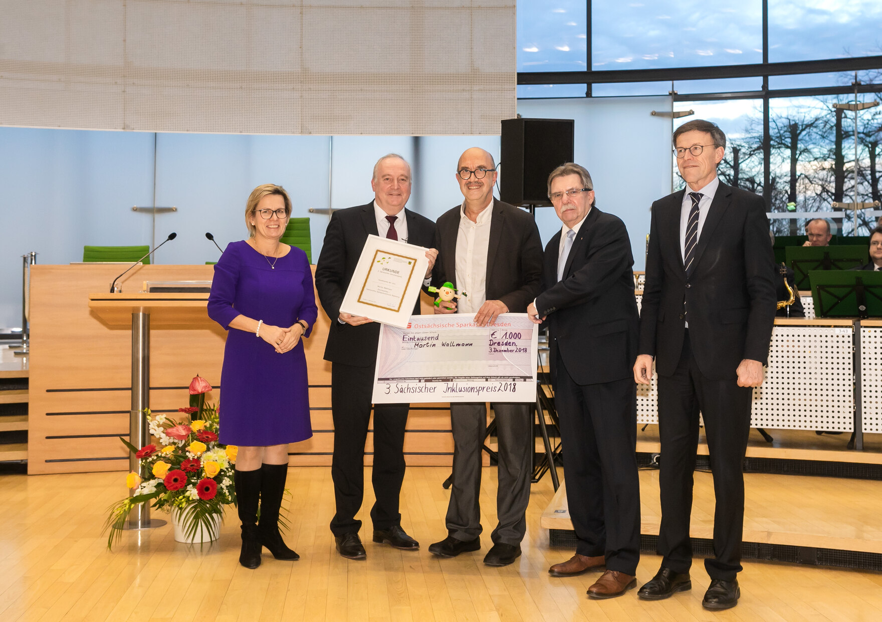 Der Preisträger steht zusammen mit dem Laudator, dem Behindertenbeauftragten, der Staatsministerin und dem Landtagspräsidenten in der Mitte des Plenarsaals des Sächsischen Landtages.