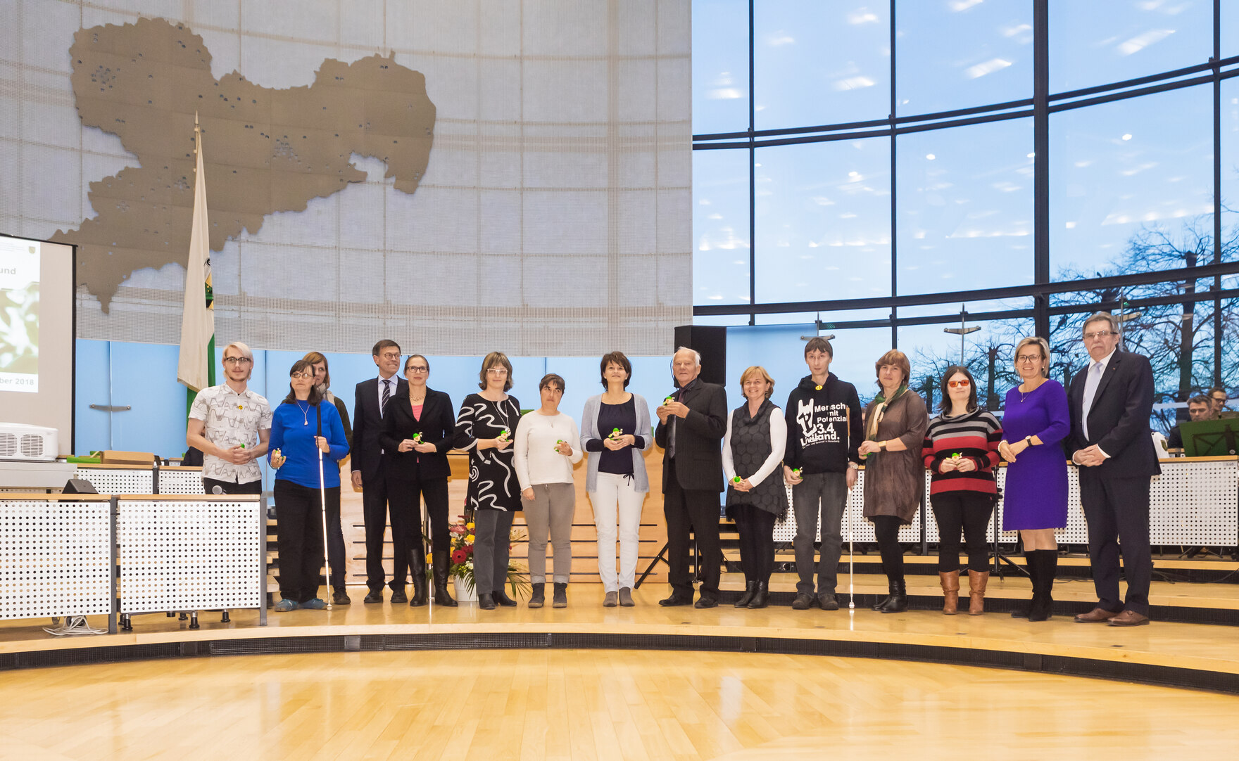 Nominierte des 3. Sächsischen Inklusionspreises stehen im Plenarsaal des Sächsischen Landtages in Dresden als Gruppe zusammen und halten ihre Auszeichnungen in den Händen. 